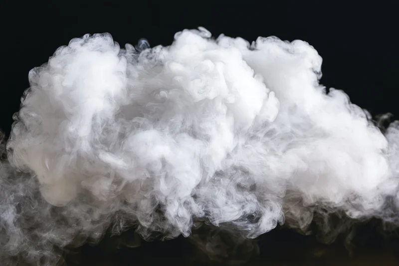 White smoke cloud drifting and dispersing midair against black background