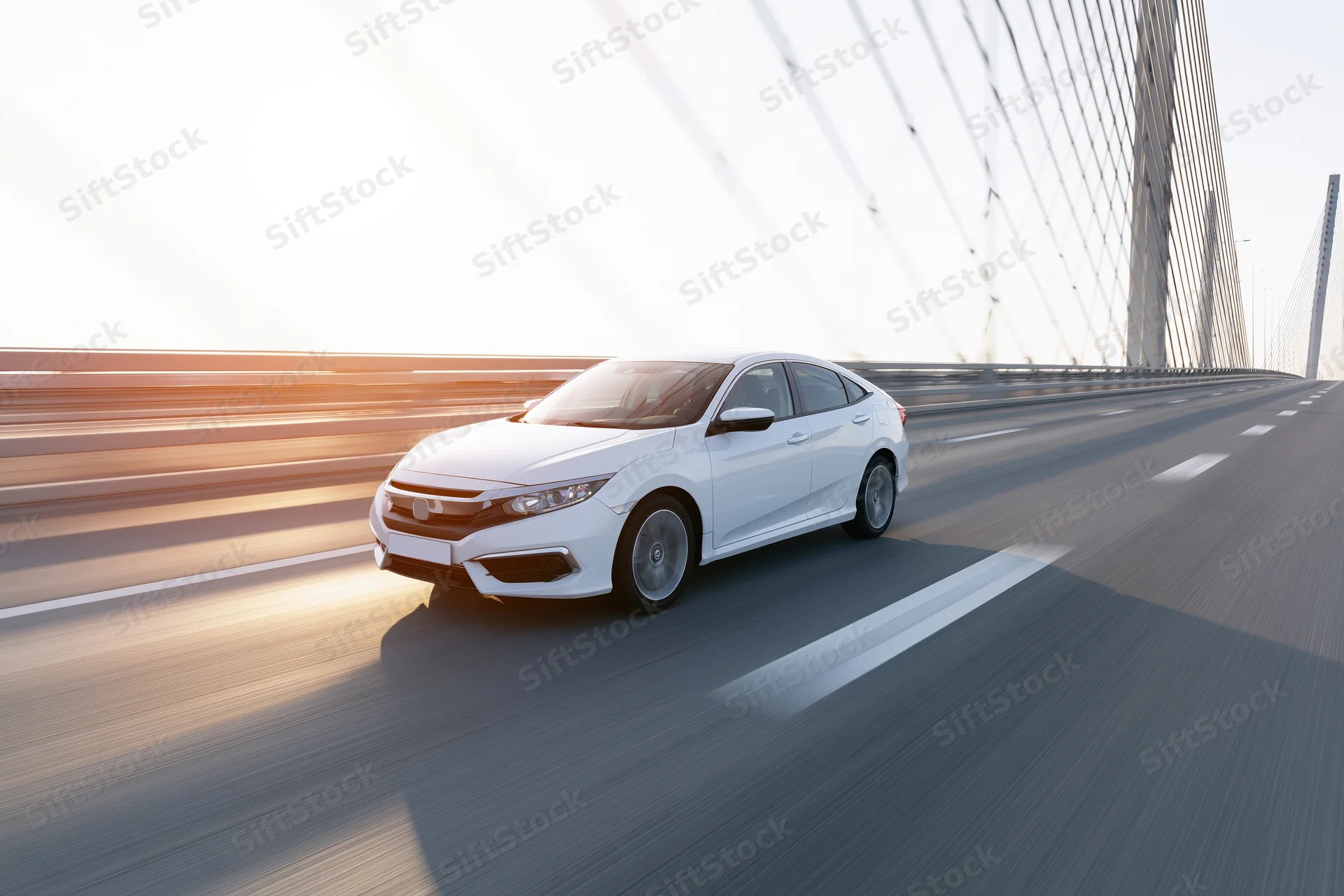 White sedan driving at speed across a cable-stayed bridge