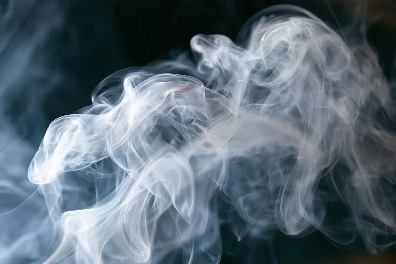 Wispy white smoke curling and swirling in layered tendrils against a dark background