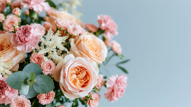 Close-up of a pink and peach floral bouquet with roses, carnations and eucalyptus against a light blue background