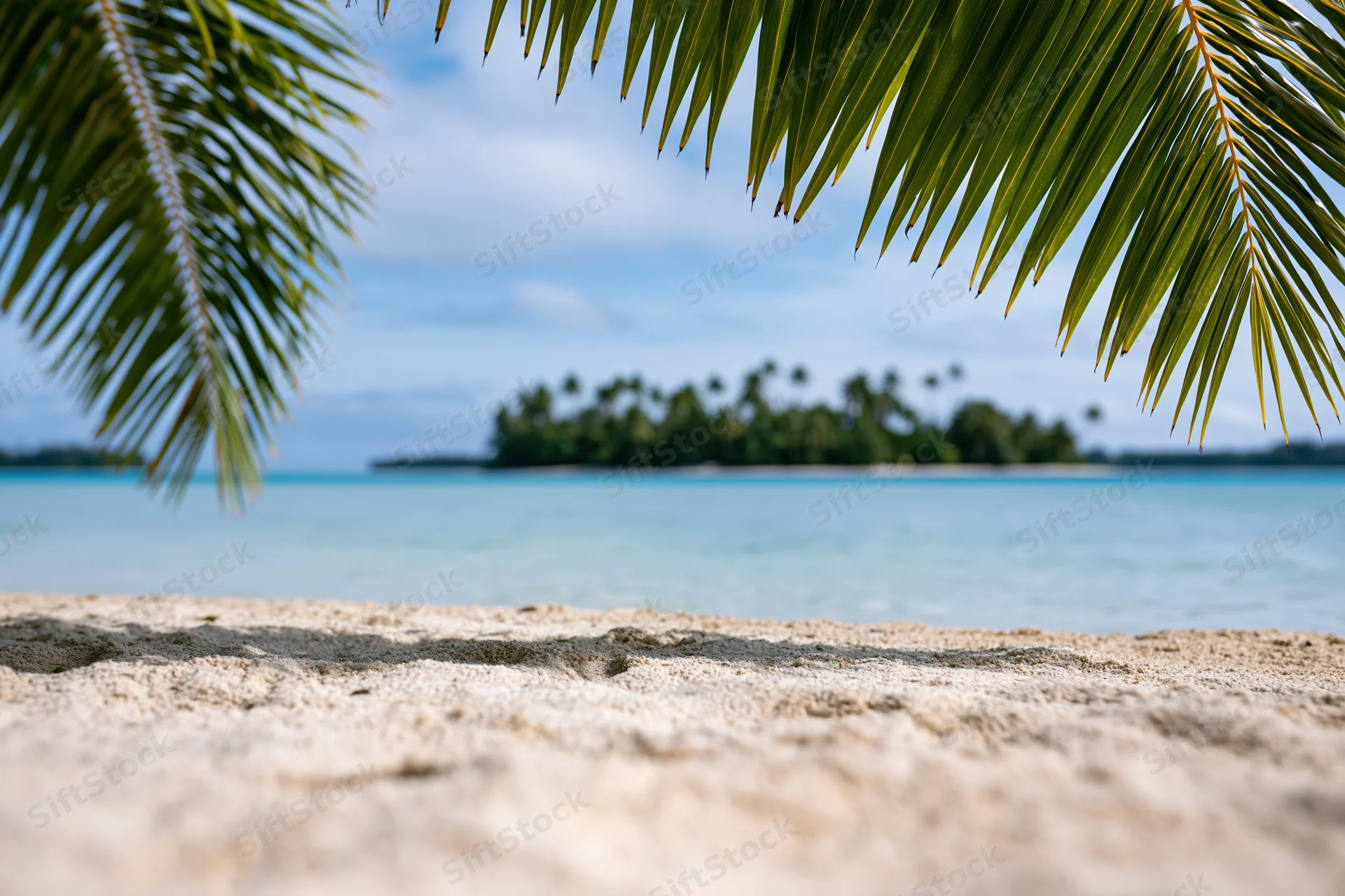 Sandy beach with palm fronds framing a distant tropical island across calm turquoise water