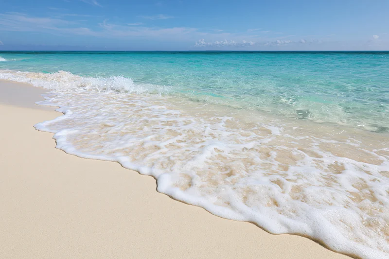 Gentle waves with white foam rolling onto golden sand at a tropical beach under a clear blue sky