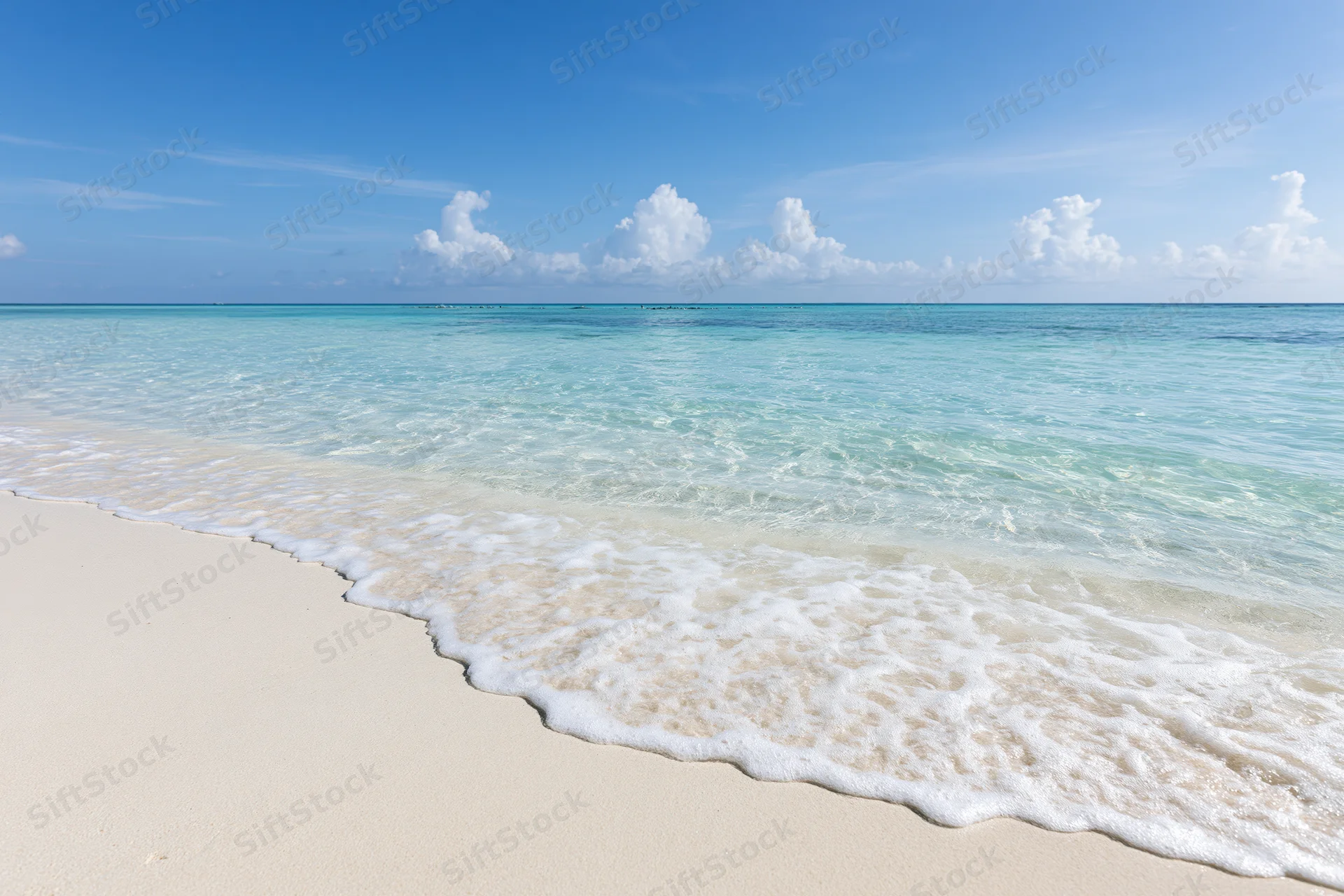 Gentle waves rolling onto white sand beach under clear blue sky with scattered clouds