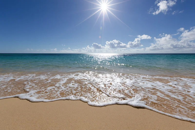 Waves washing onto sandy beach under bright sun and blue sky