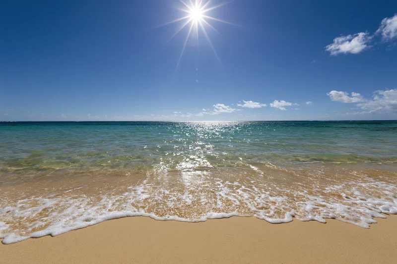 Gentle waves rolling onto golden sand under bright sun at tropical beach