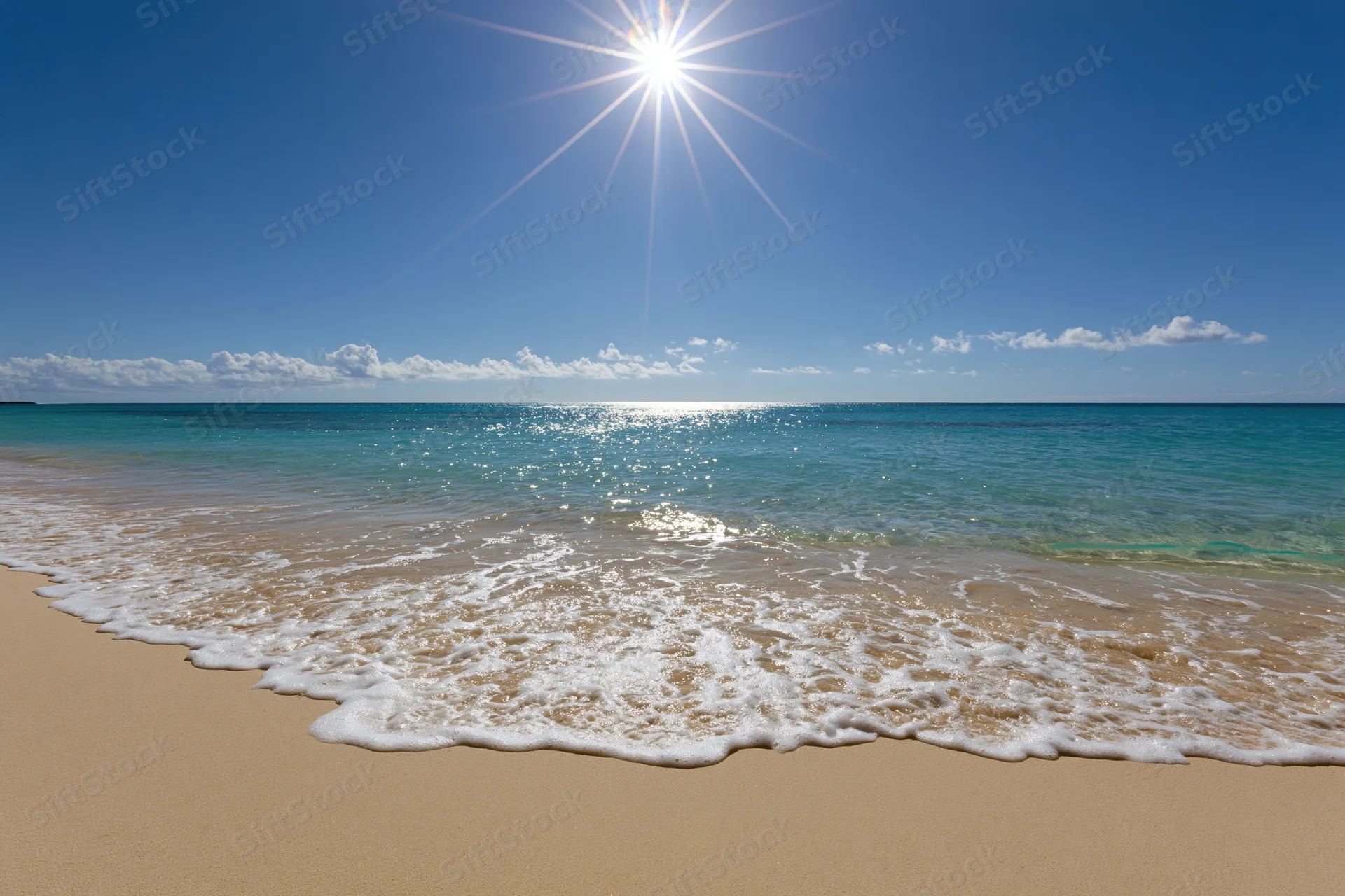 Gentle waves rolling onto a sandy beach under bright sunlight with clear blue sky and ocean horizon