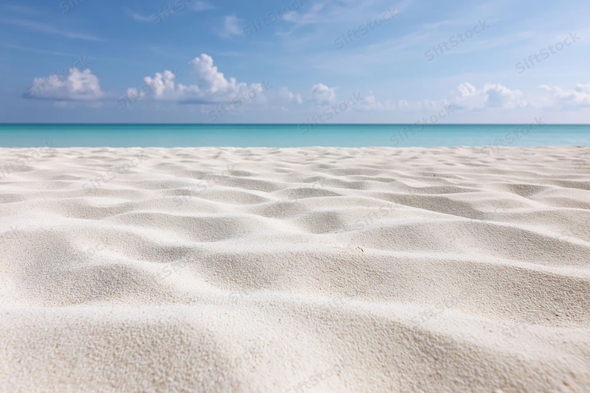 Rippled white sand on a tropical beach with turquoise ocean and blue sky in the background