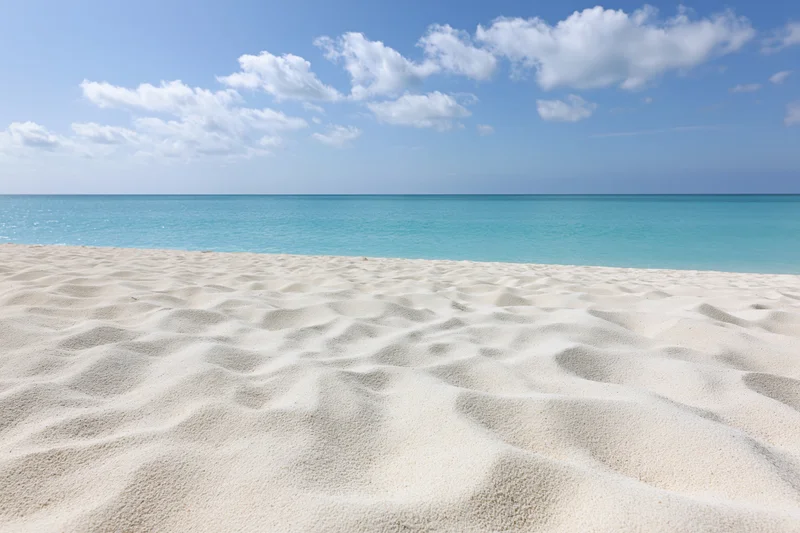 White sandy beach meeting turquoise ocean under blue sky with scattered clouds