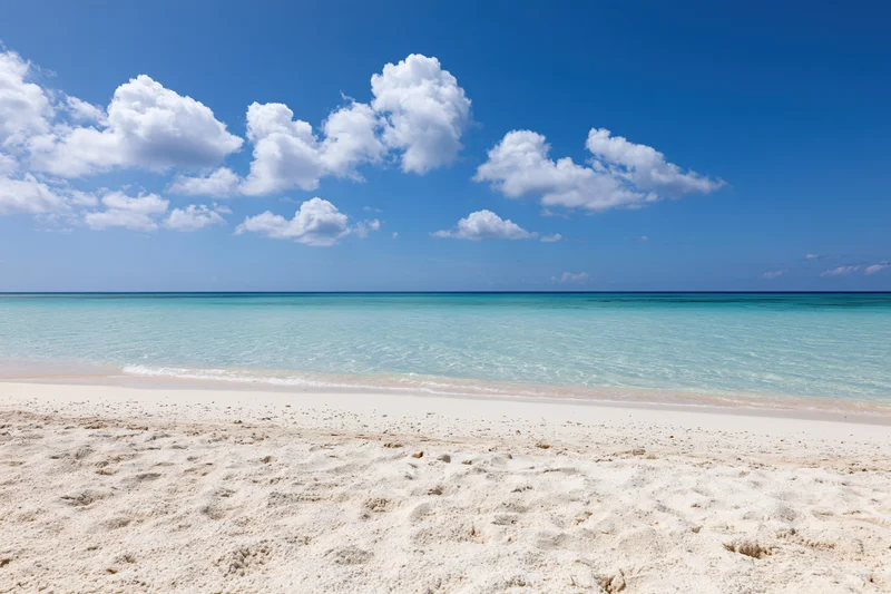 White sandy beach meeting turquoise ocean under bright blue sky with scattered clouds