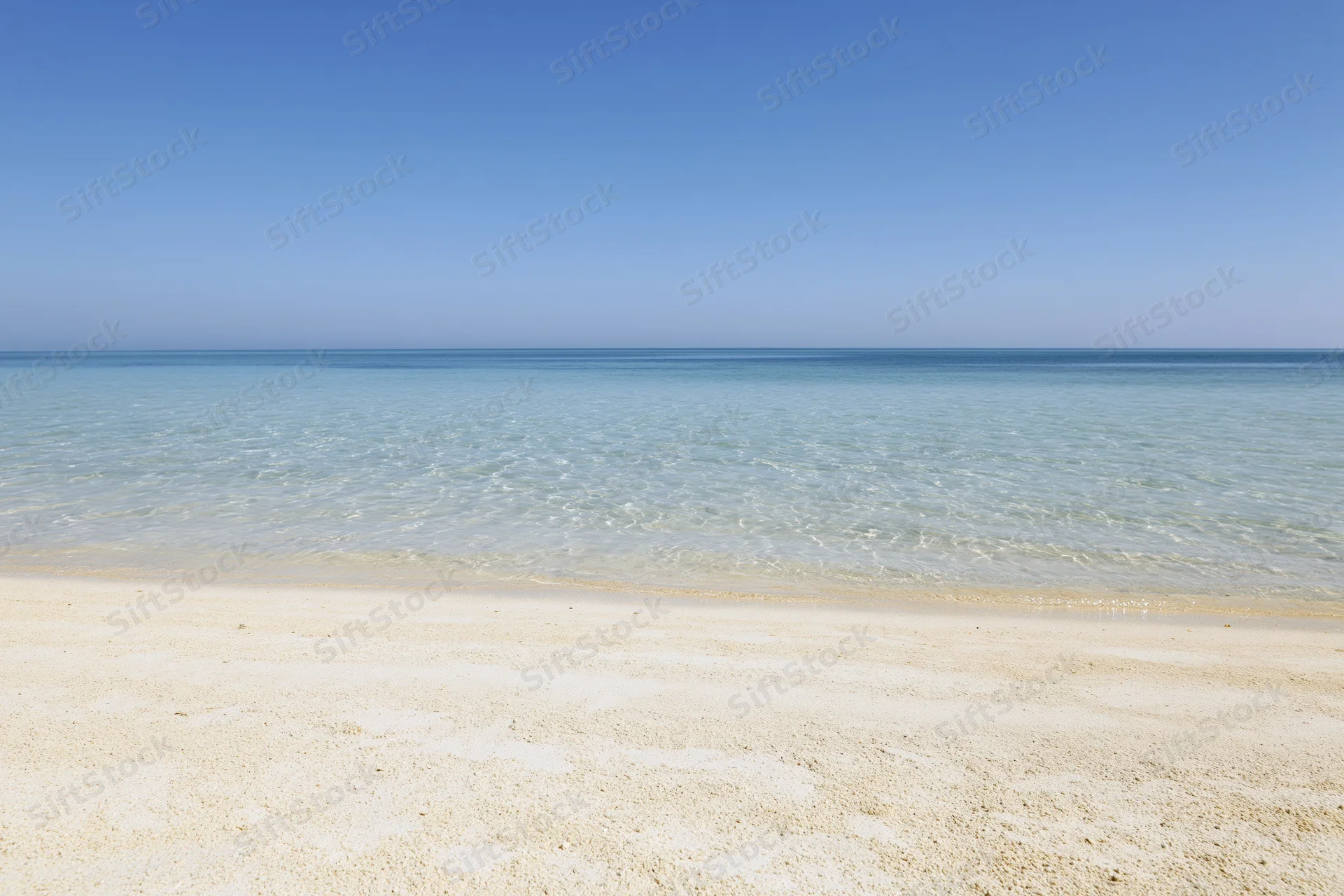 Calm ocean meeting white sand beach under clear blue sky