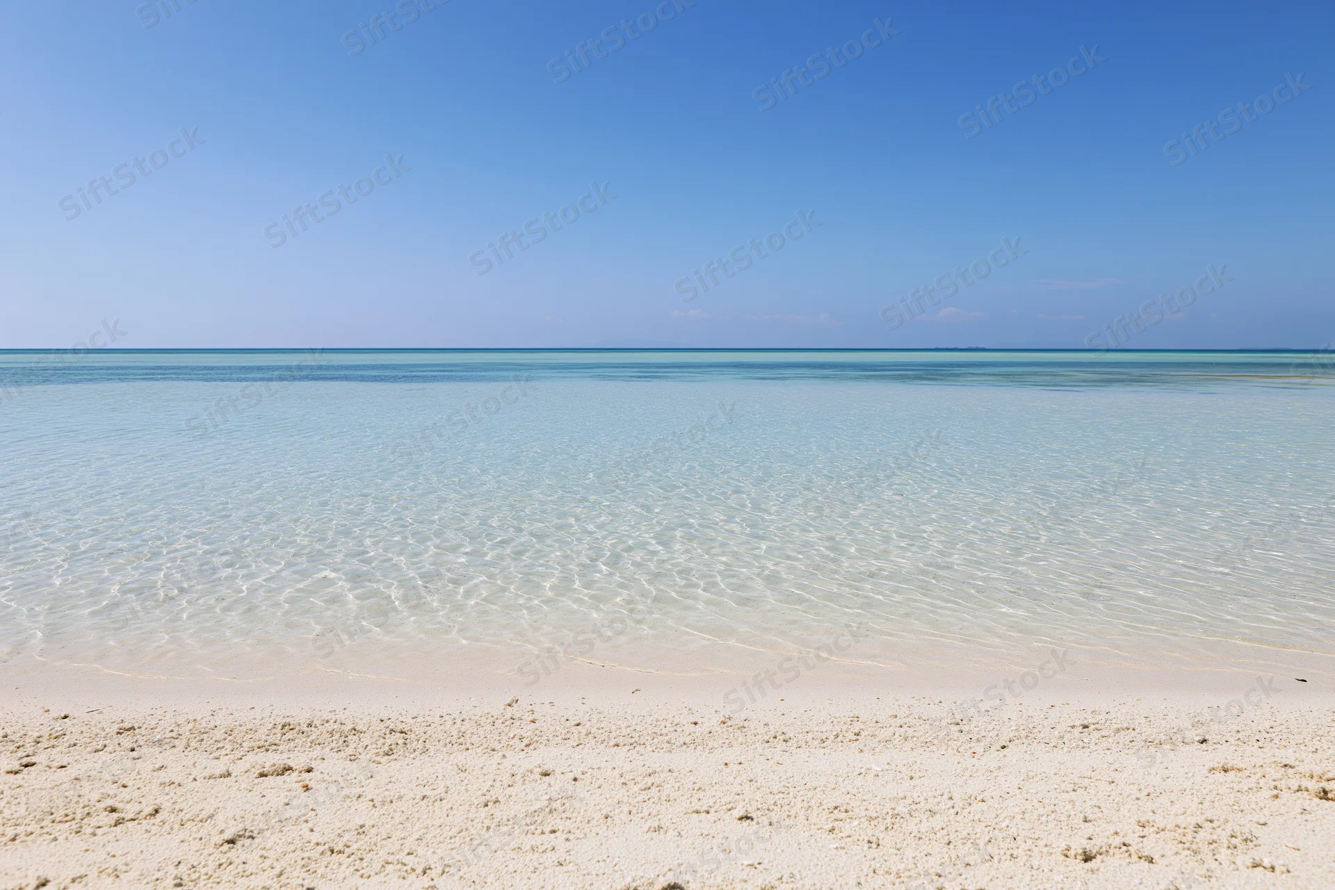 Clear turquoise water meeting white sand beach under blue sky at calm shoreline