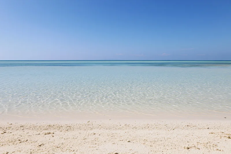 Clear turquoise water meeting white sand beach under blue sky at calm shoreline