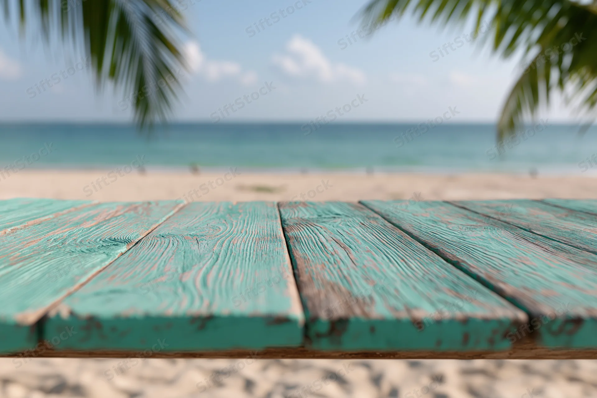 Weathered turquoise wooden table on sandy beach with ocean and palm fronds in background