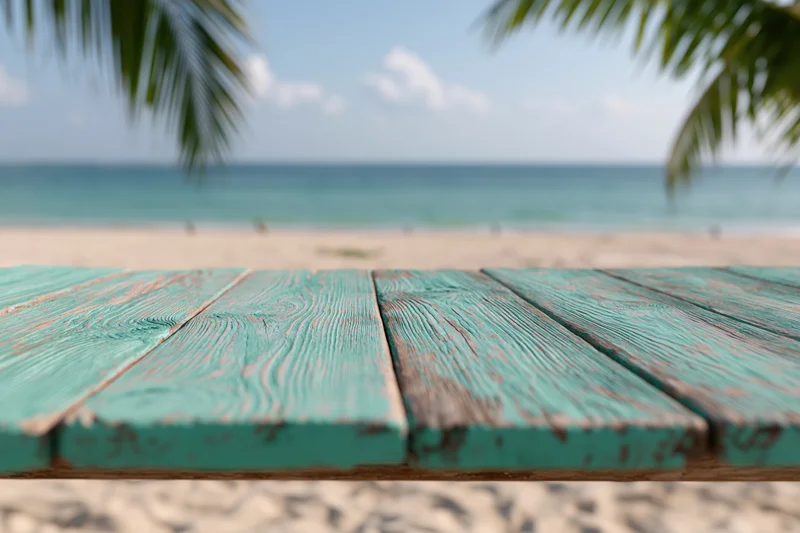 Weathered turquoise wooden table on sandy beach with ocean and palm fronds in background
