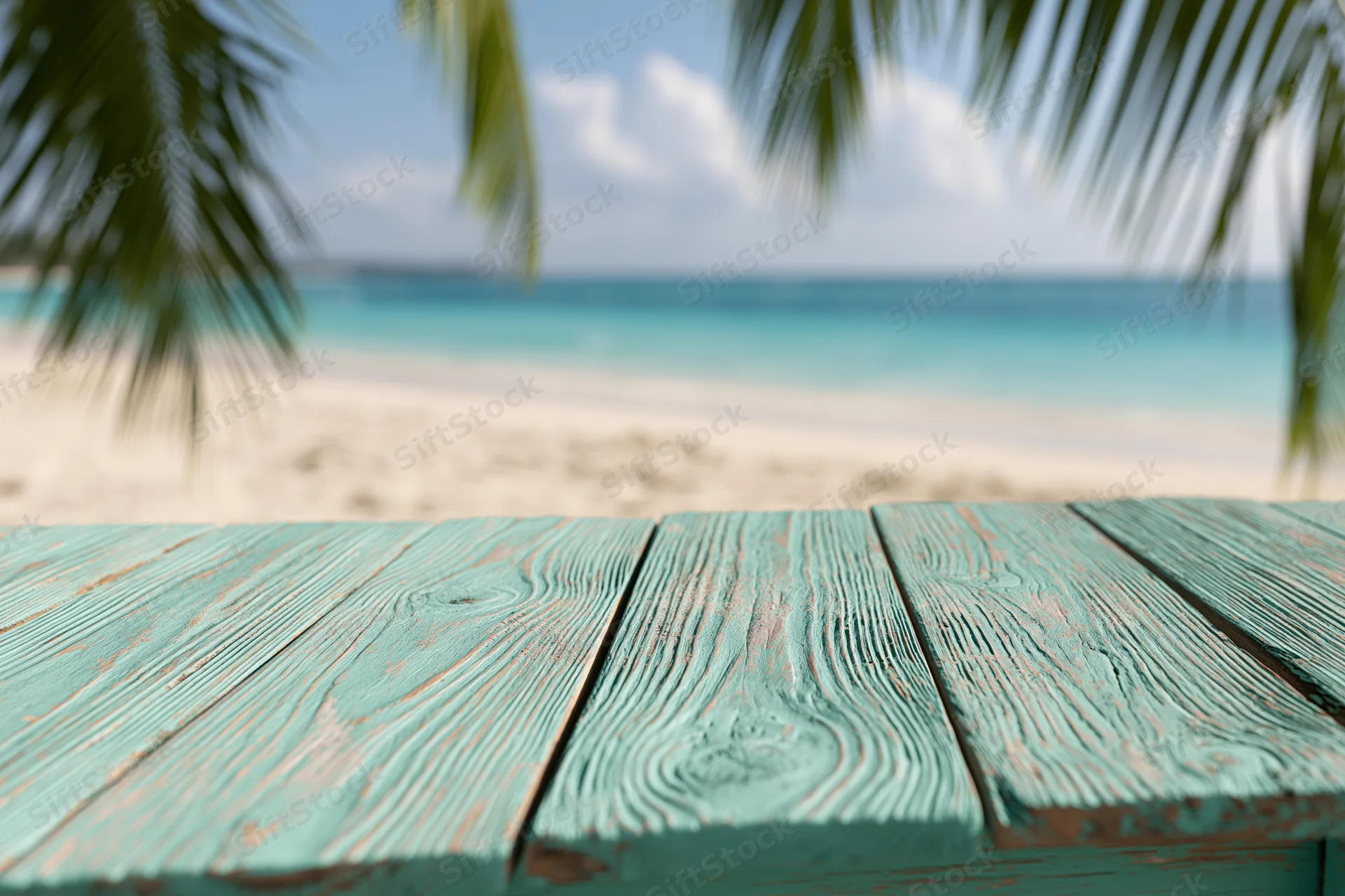 Weathered turquoise wooden table overlooking a tropical beach with palm fronds and ocean in the background