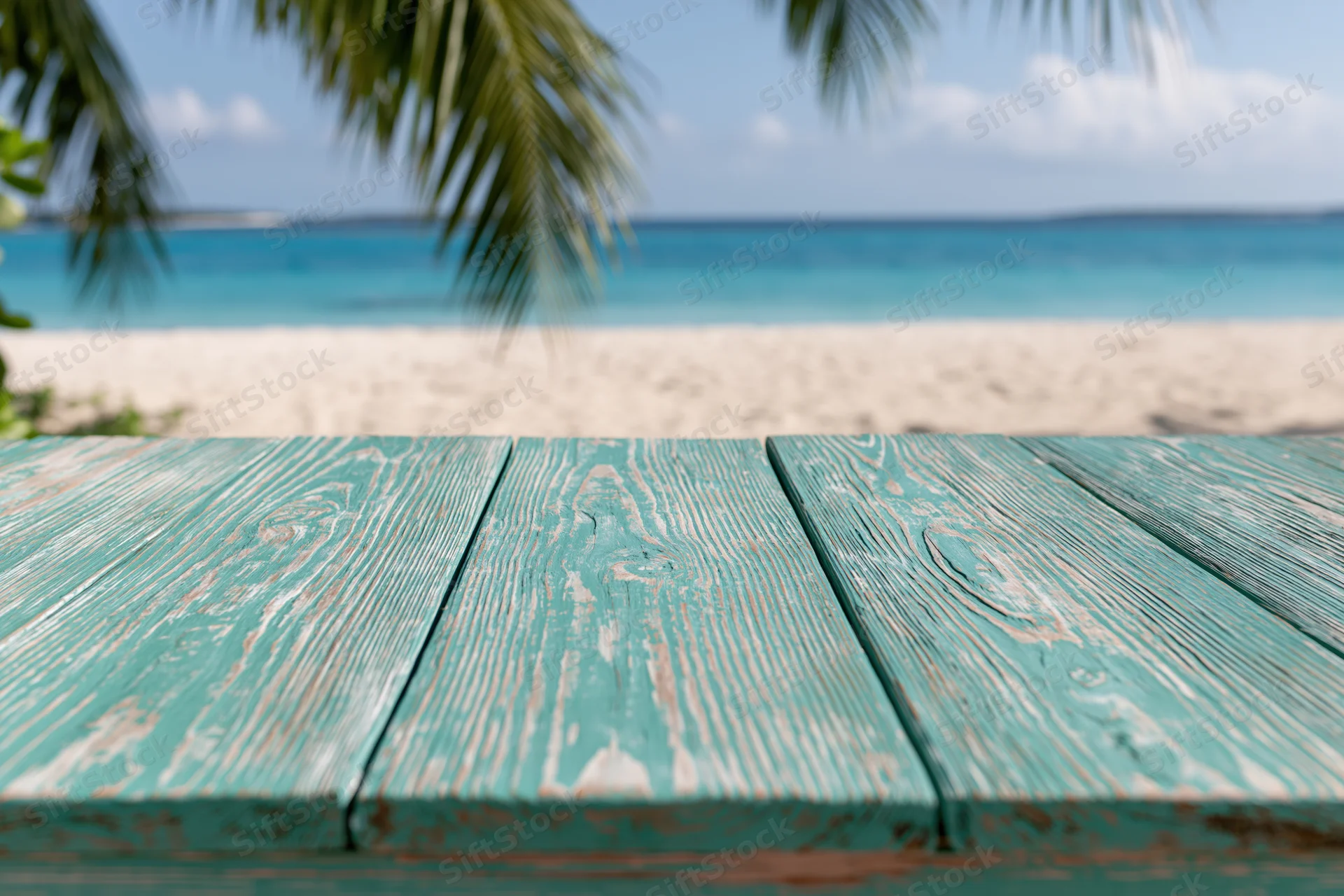Weathered turquoise wooden table on a sandy beach overlooking the ocean with palm fronds above