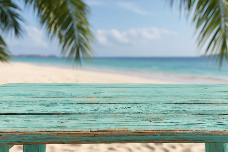 Turquoise wooden table on a sandy beach with palm fronds and ocean in the background