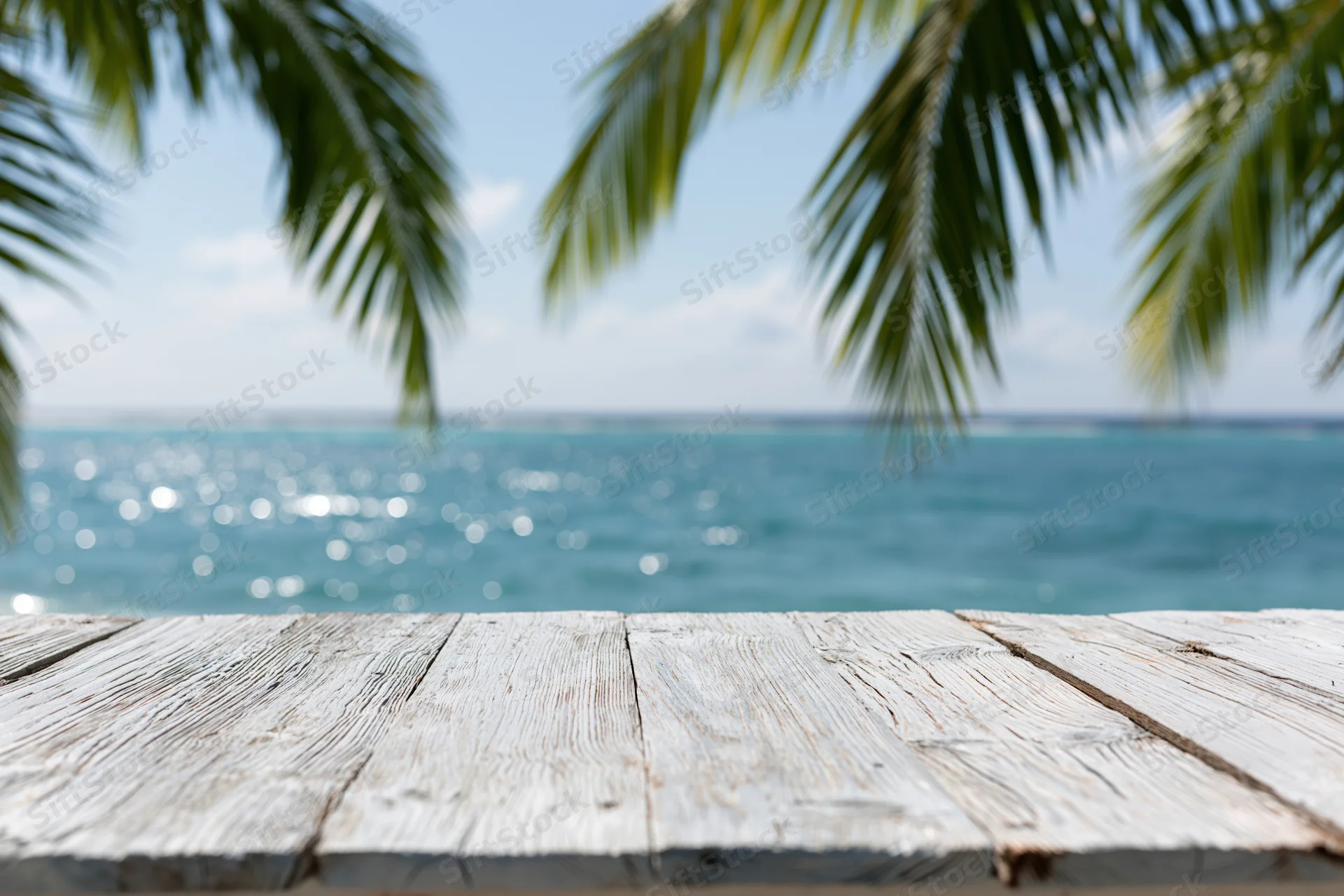 Weathered wooden table in front of ocean view with palm fronds overhead