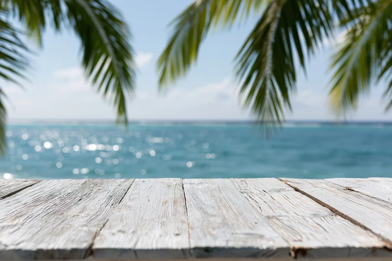 Weathered wooden table in front of ocean view with palm fronds overhead
