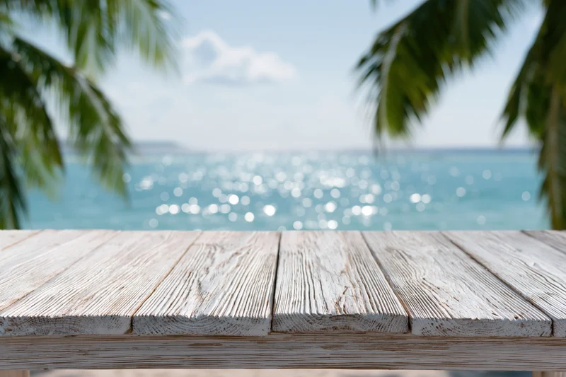 Weathered wooden table in front of a tropical beach with ocean and palm trees in the background