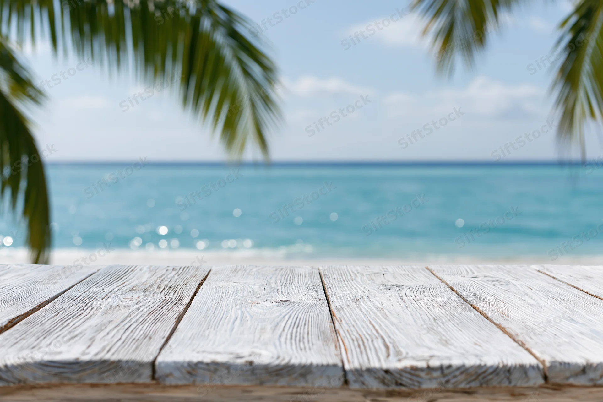 Weathered wooden table overlooking turquoise ocean with palm fronds framing the view