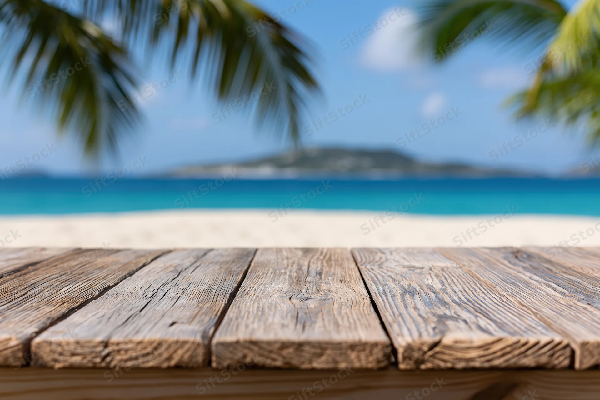 Wooden table on a tropical beach overlooking the ocean with palm trees and distant island