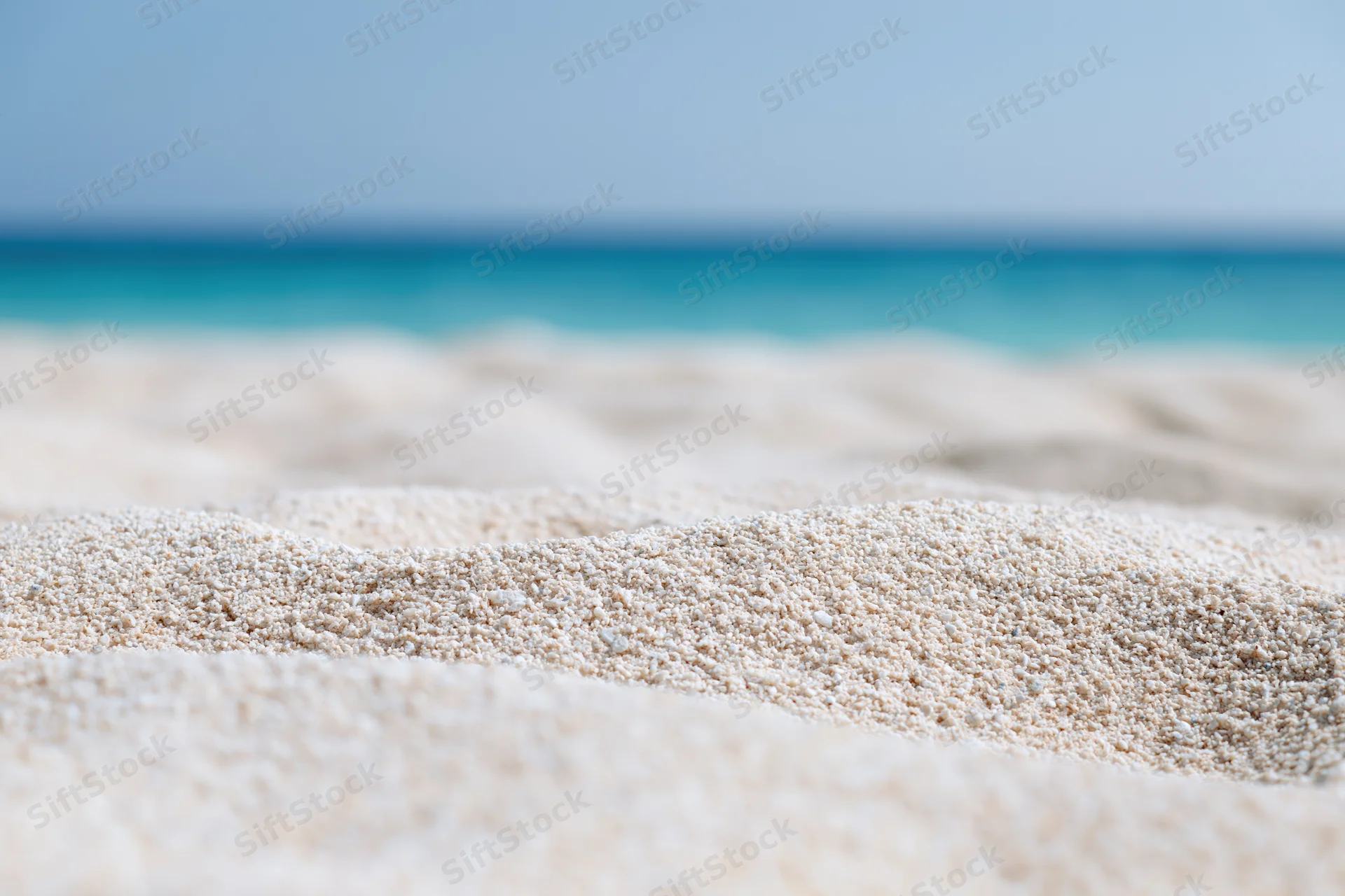 Closeup of white sand on a beach with turquoise ocean in the background