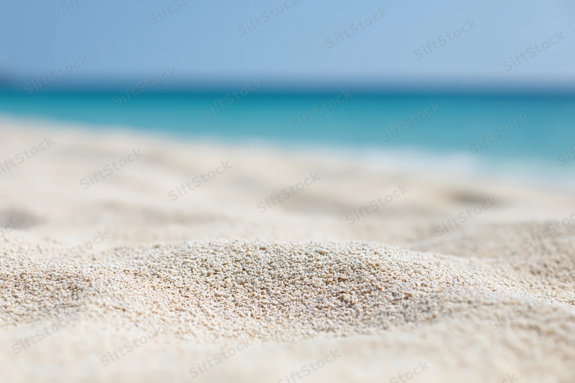 Close-up of textured white sand on a beach with turquoise ocean in the background