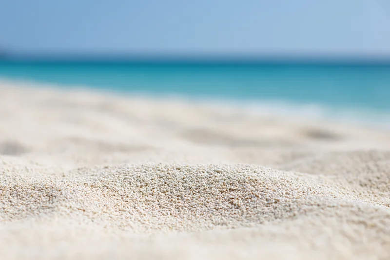 Close-up of textured white sand on a beach with turquoise ocean in the background
