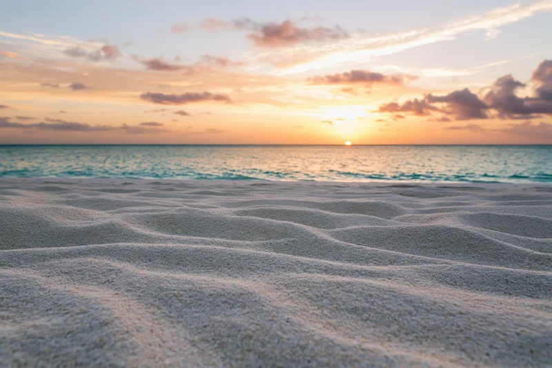 Sunset over ocean with rippled sand in foreground at twilight