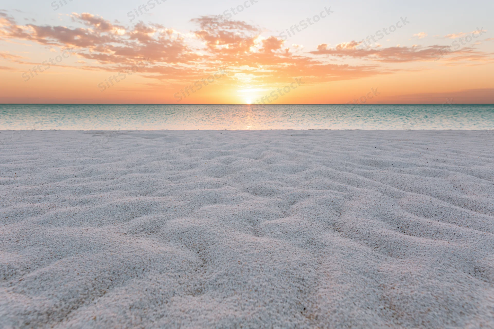 Sunset over calm ocean with rippled white sand in foreground