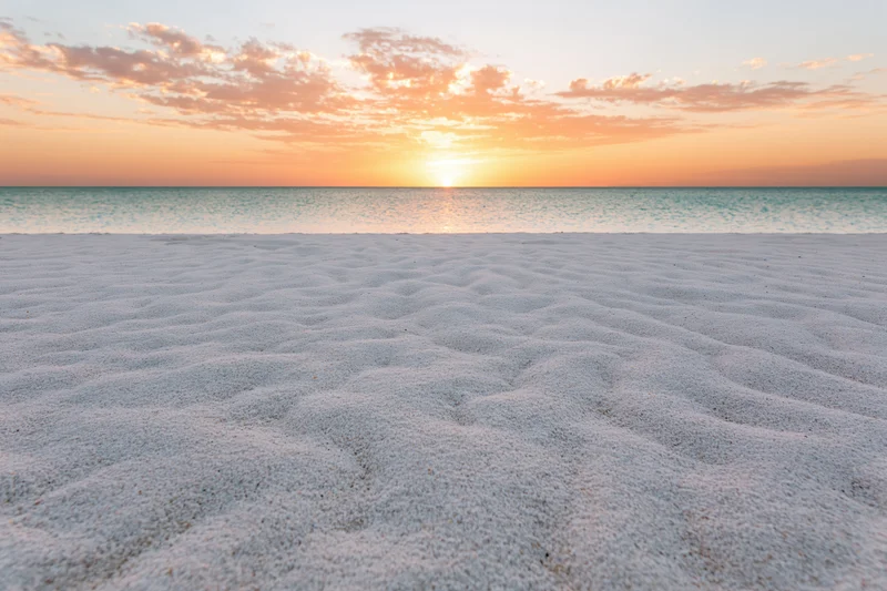 Sunset over calm ocean with rippled white sand in foreground