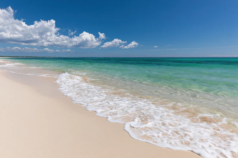 Gentle waves rolling onto a sandy beach under a clear blue sky with scattered clouds
