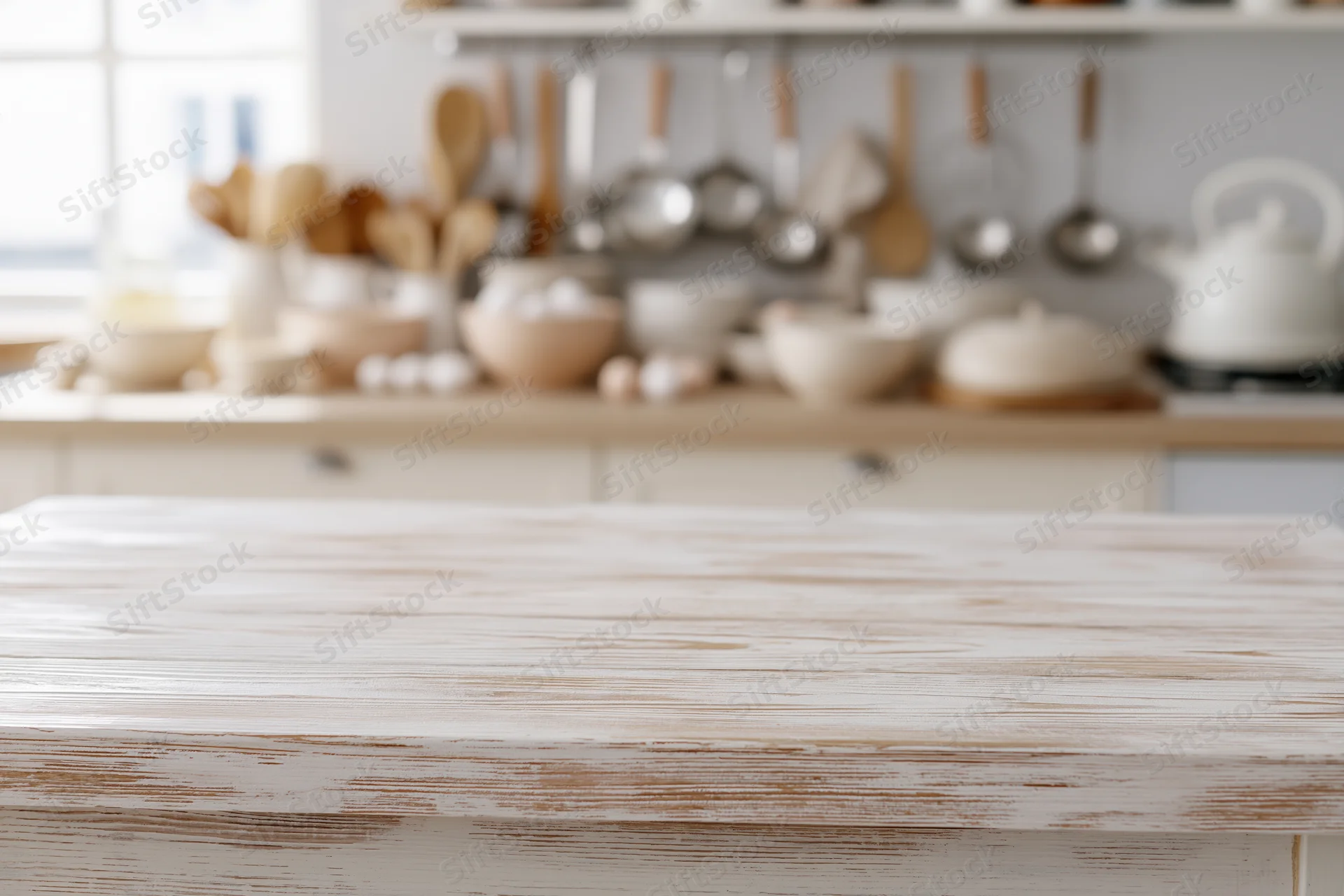 White-washed wooden kitchen countertop in a rustic farmhouse kitchen with cooking utensils and ceramic bowls in the background