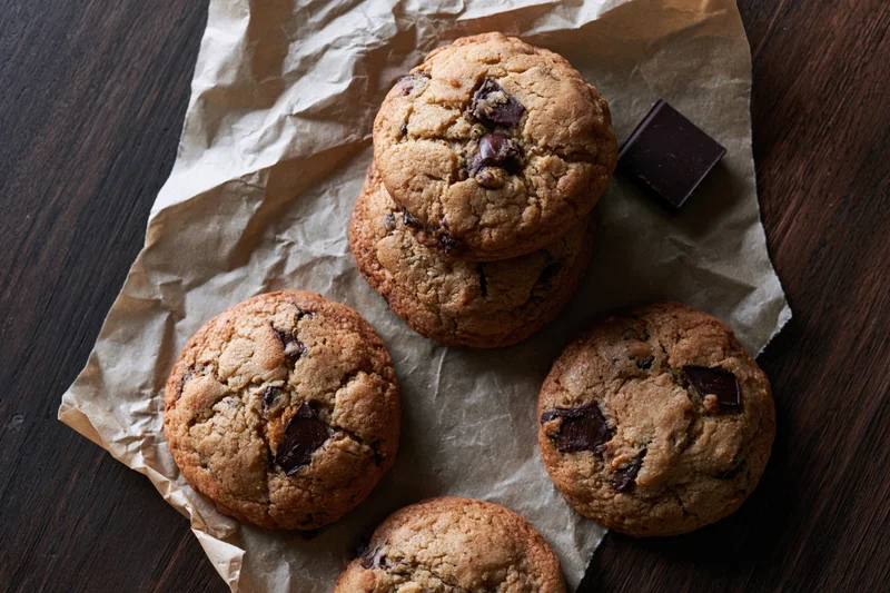 Chocolate chip cookies arranged on crumpled parchment paper on a dark wooden table