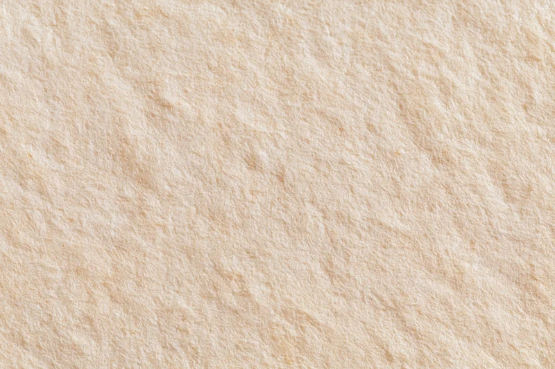 Closeup of beige textured paper surface with subtle fibrous grain and matte finish