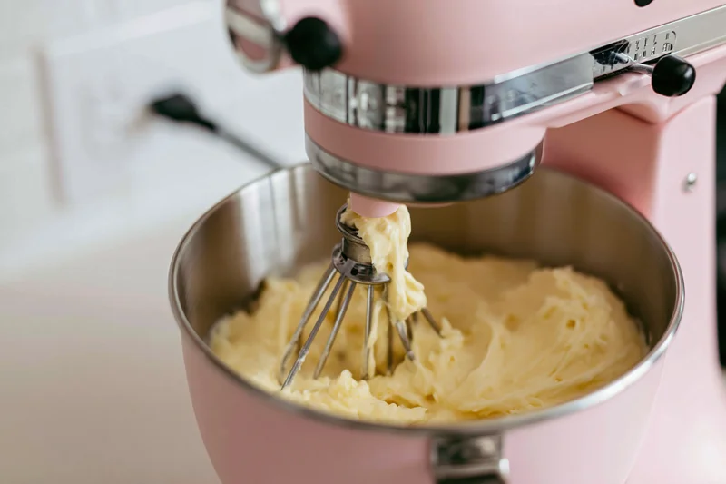Pink stand mixer creaming butter in a stainless steel bowl on a kitchen counter