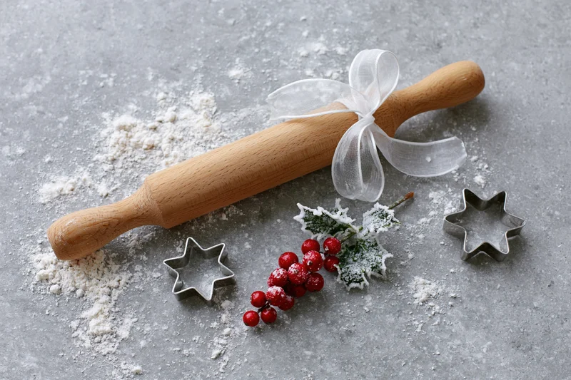 Wooden rolling pin with star cookie cutters and holly berries on floured gray surface