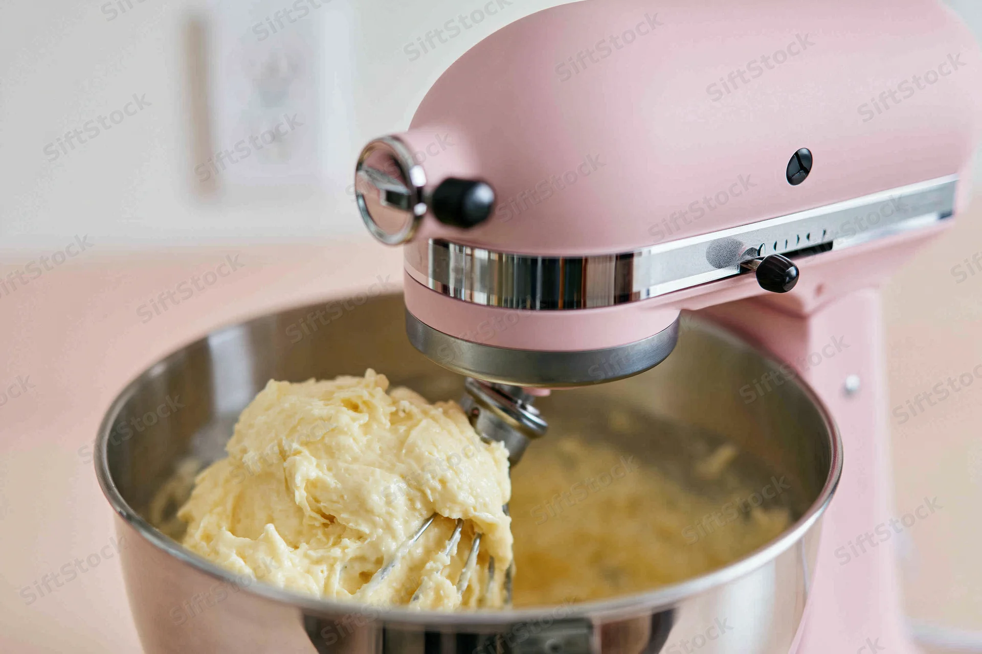 Pink stand mixer creaming dough in stainless steel bowl on kitchen counter