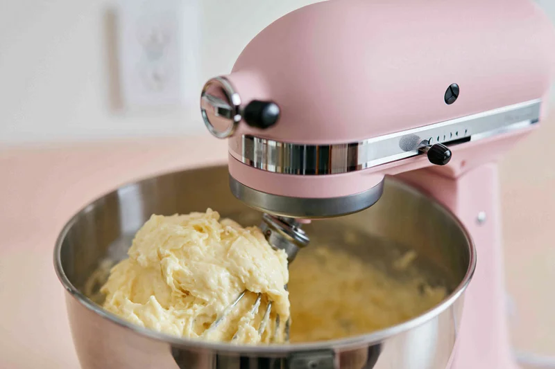 Pink stand mixer creaming dough in stainless steel bowl on kitchen counter