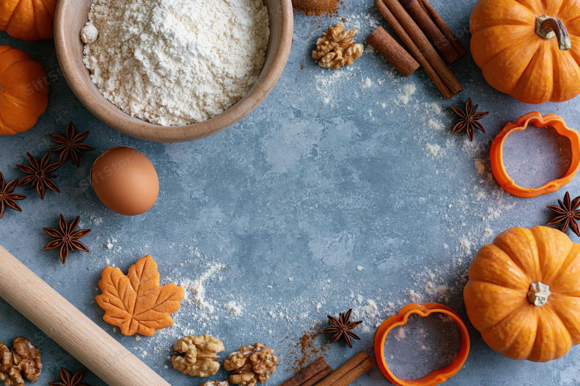 Pumpkin baking ingredients arranged on a gray countertop with cookie cutters and spices