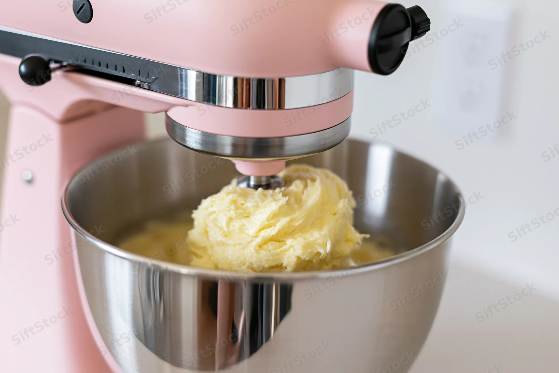 Pink stand mixer whipping butter cream in stainless steel bowl on kitchen counter