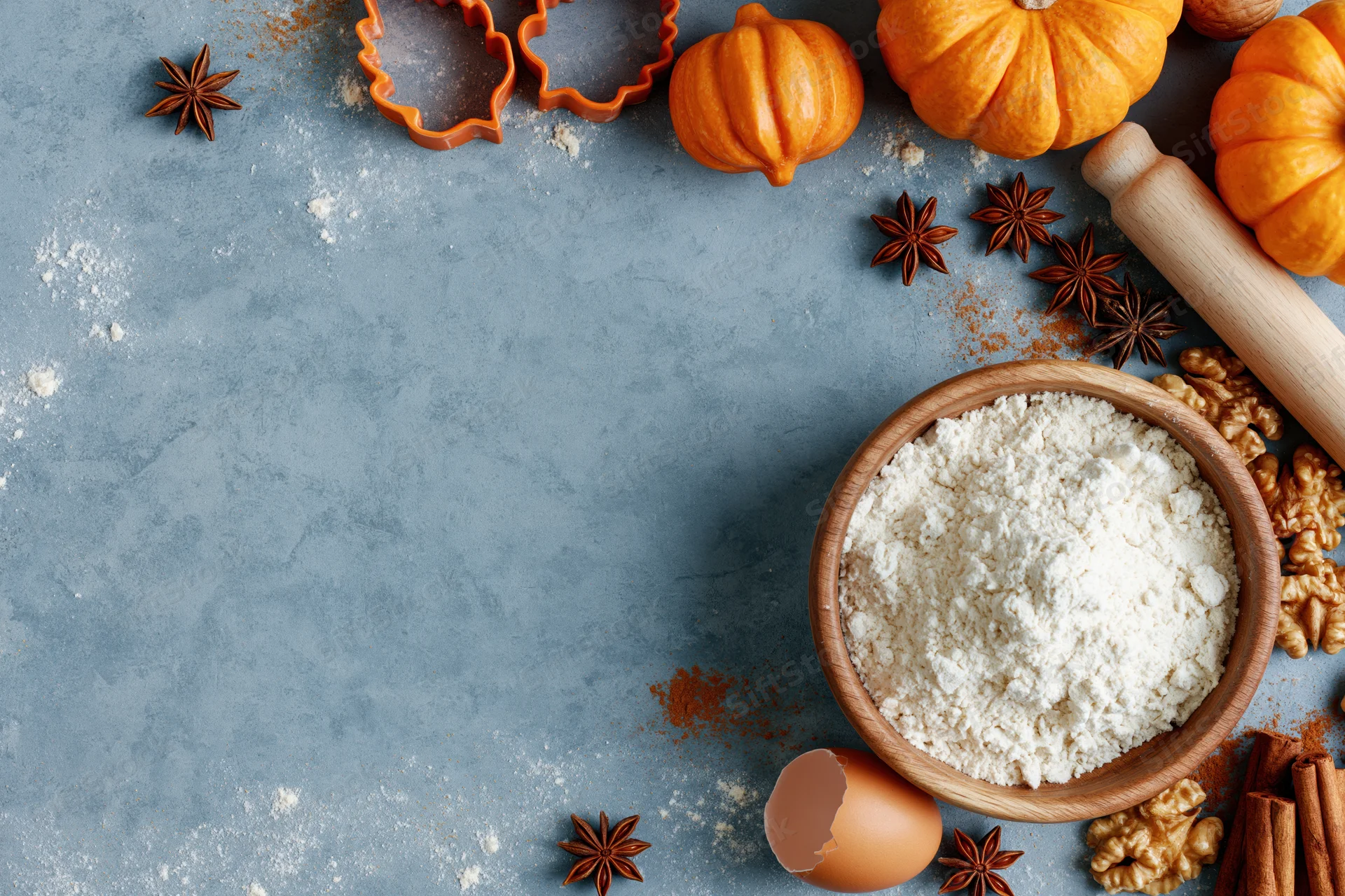 Baking ingredients arranged on a gray countertop with pumpkins, spices and cookie cutters for autumn cooking