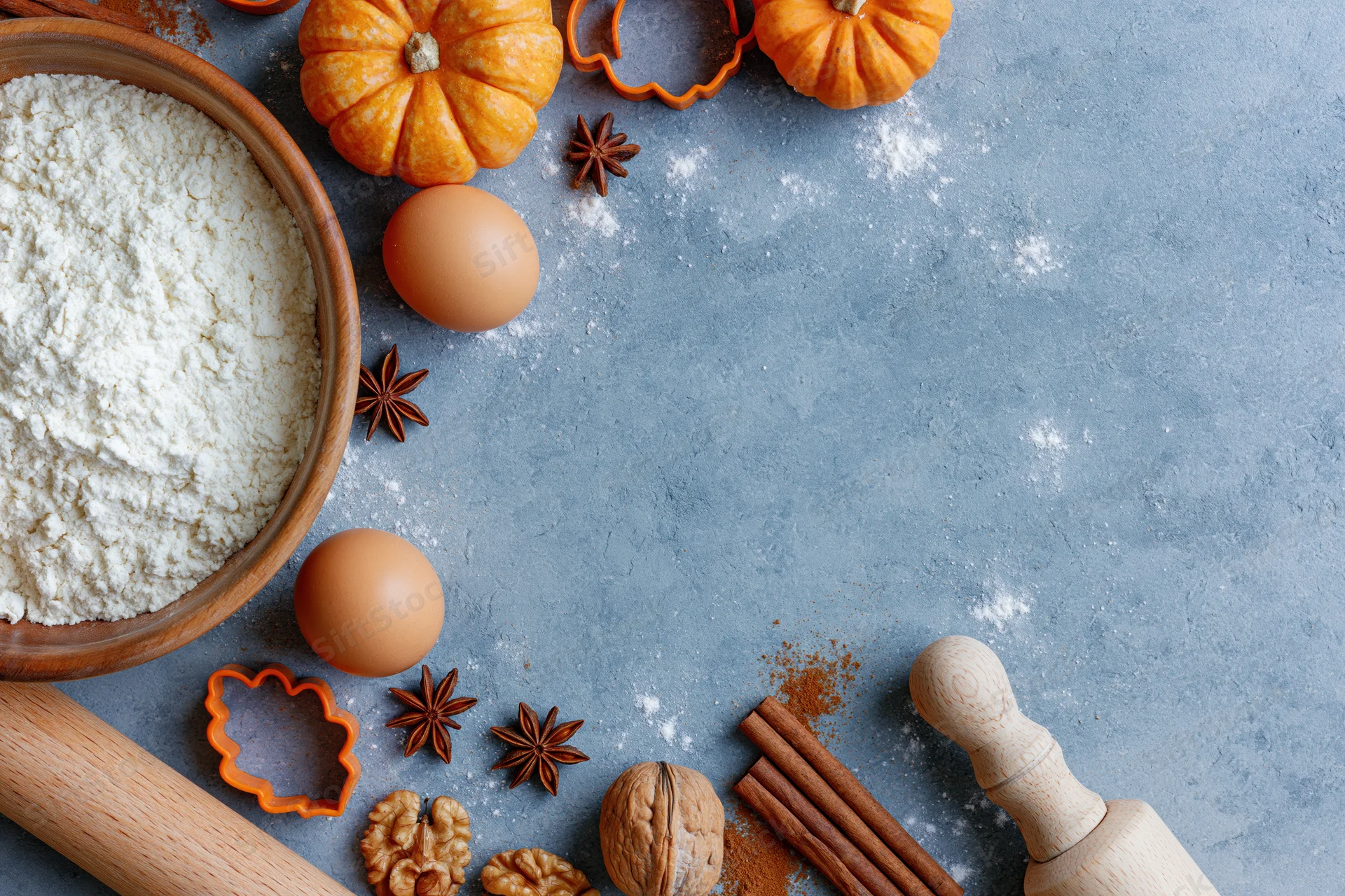 Baking ingredients arranged on a gray countertop with pumpkins and spices for autumn dessert preparation