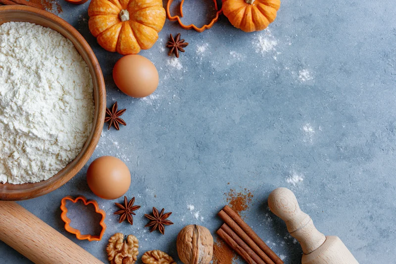 Baking ingredients arranged on a gray countertop with pumpkins and spices for autumn dessert preparation