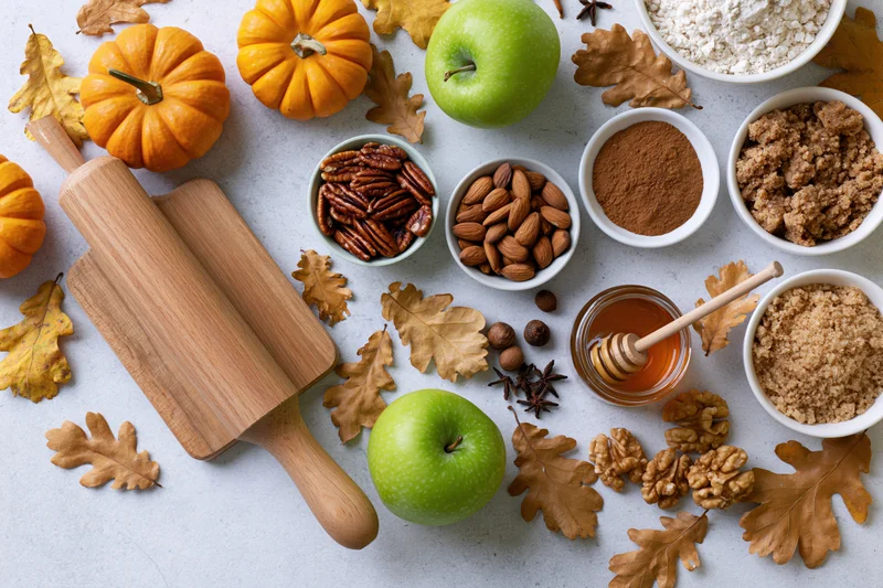 Autumn baking ingredients arranged on a white surface with pumpkins, apples, nuts, spices and a wooden rolling pin