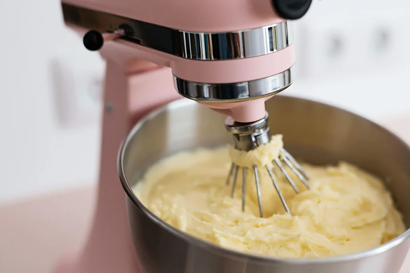 Pink stand mixer creaming butter in a stainless steel bowl on a kitchen counter