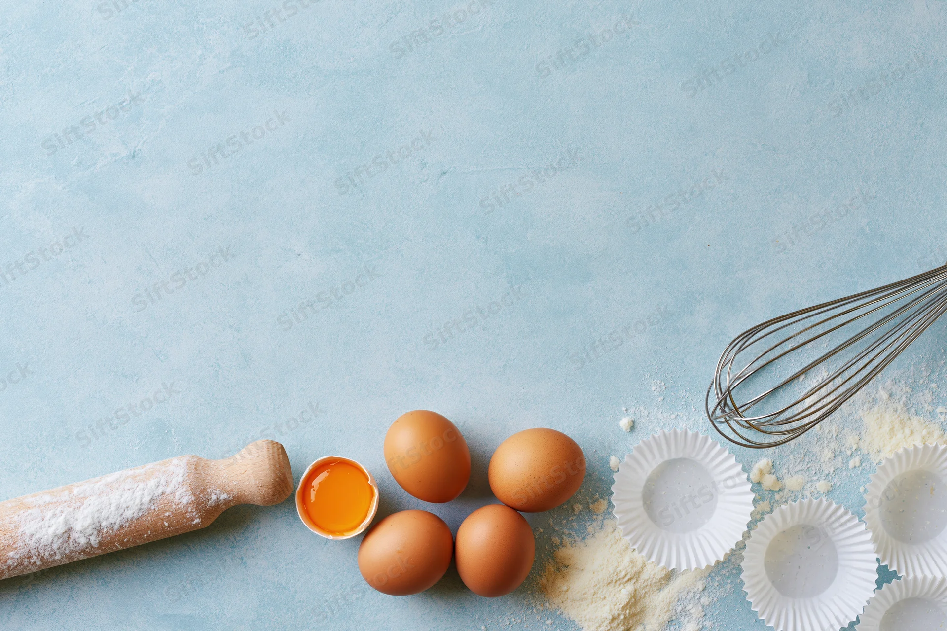 Eggs and baking tools arranged on a blue surface with copyspace