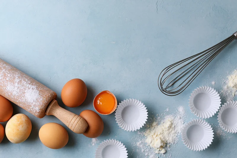 Baking ingredients and tools arranged on a blue surface with copyspace
