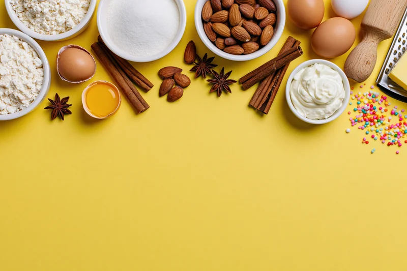 Baking ingredients arranged along top of yellow surface with copyspace below